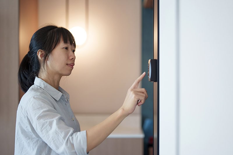 Young woman adjusting thermostat mounted on the wall.