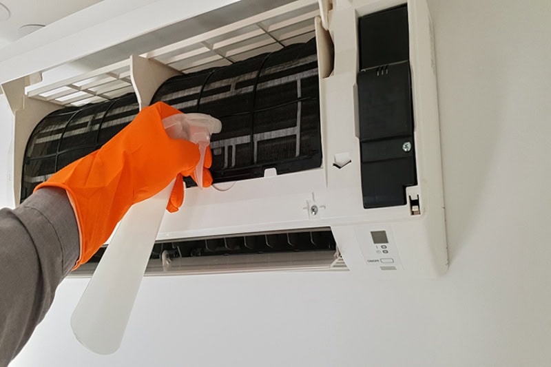 Photo of a hand in a rubber glove cleaning an AC unit.