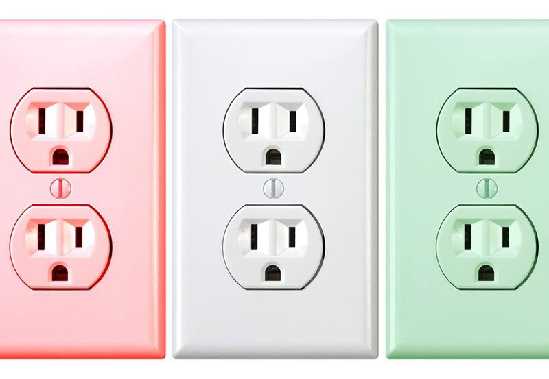 Three standard dual electrical wall outlets lined upside by side, colored in light red, white, and light green against a plain background.