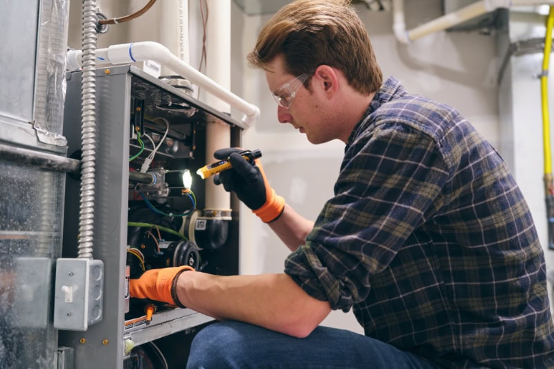 Schedule Your Annual Furnace Inspection Now. A repairman working inside a home, repairing a furnace.